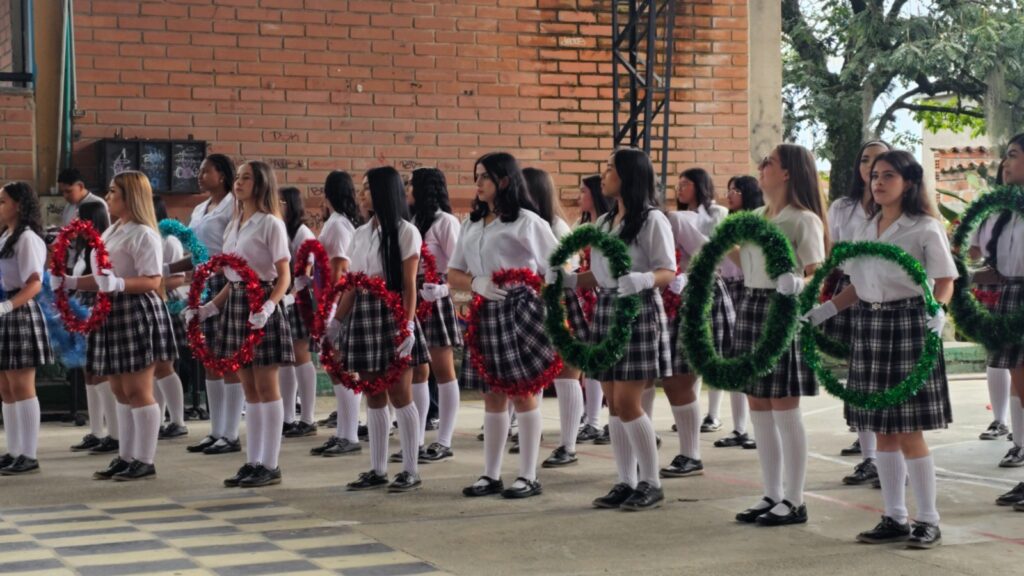 Estudiantes en formación sosteniendo aros decorados con guirnaldas verdes y rojas durante un acto cívico